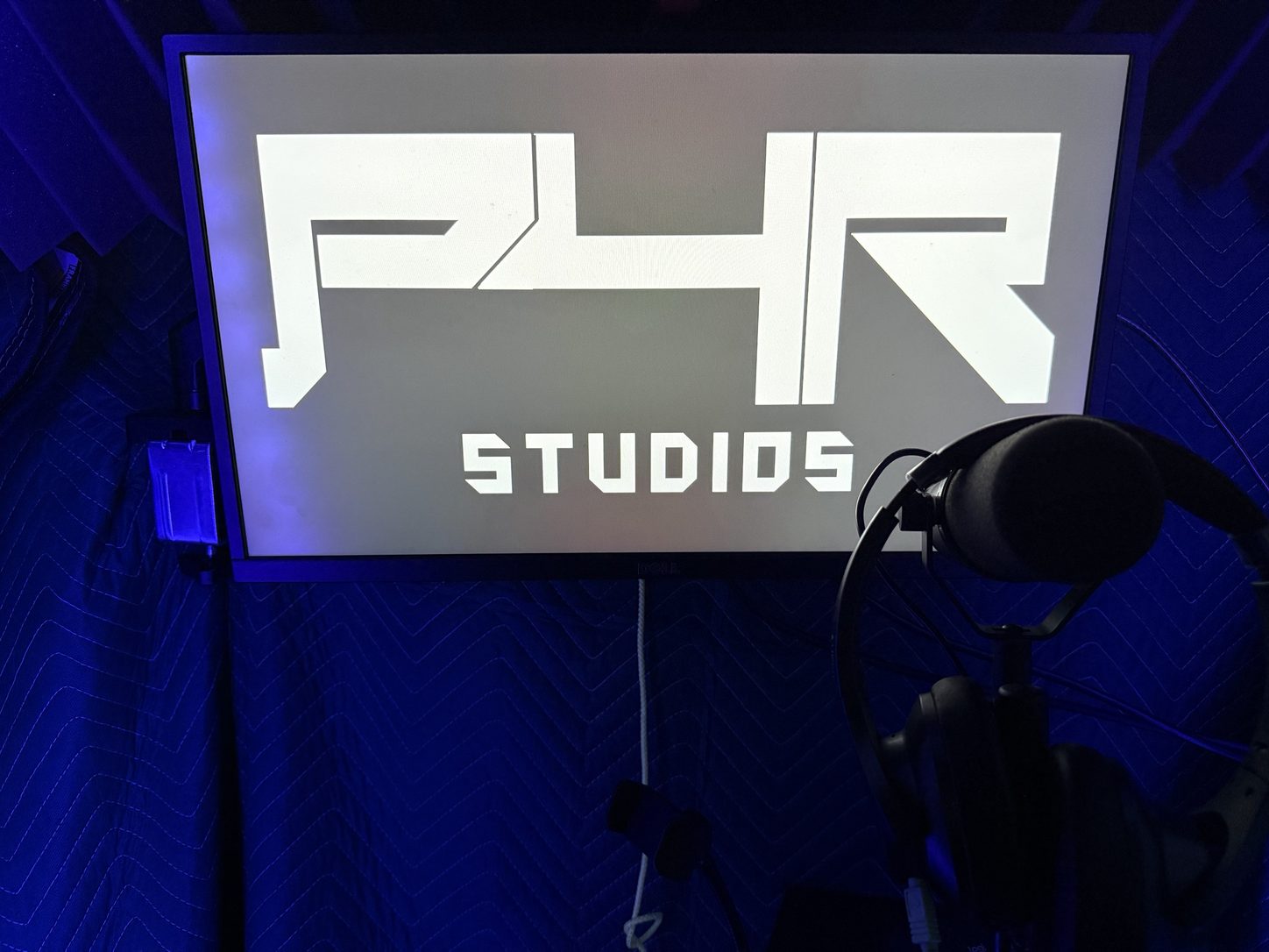 The P4R Studios vocal booth: a microphone and headphones in front of a monitor showing the P4R Studios logo, lit blue